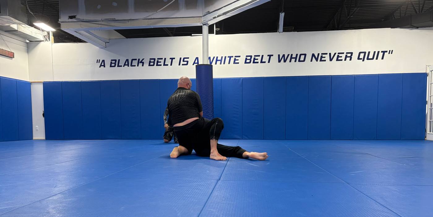 Two students training on the blue mat under the academy slogan